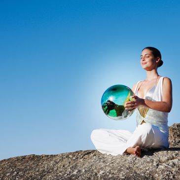Woman meditating outdoors holding a reflective sphere.
