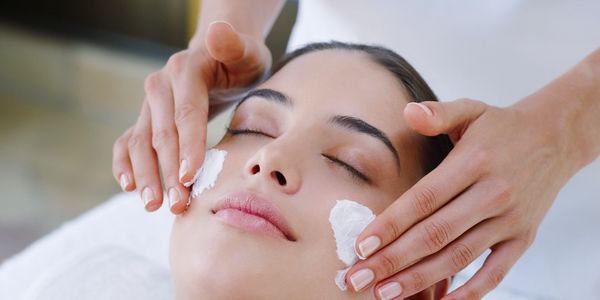 Woman receiving a facial cream treatment with eyes closed.