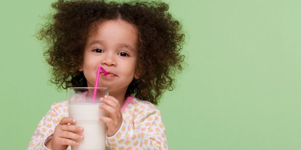 Niña bebiendo un vaso de leche con una pajilla rosada.