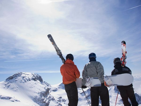 Three skiers overlooking snowy mountains.