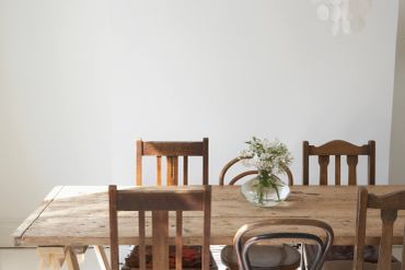 Rustic wooden table with mismatched chairs and a vase of flowers.