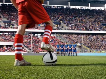 Soccer player preparing for a free kick in a crowded stadium.