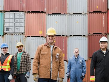 Diverse group of workers standing in front of stacked shipping containers.