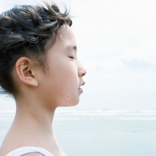 A young girl with braided hair meditates peacefully by the sea.