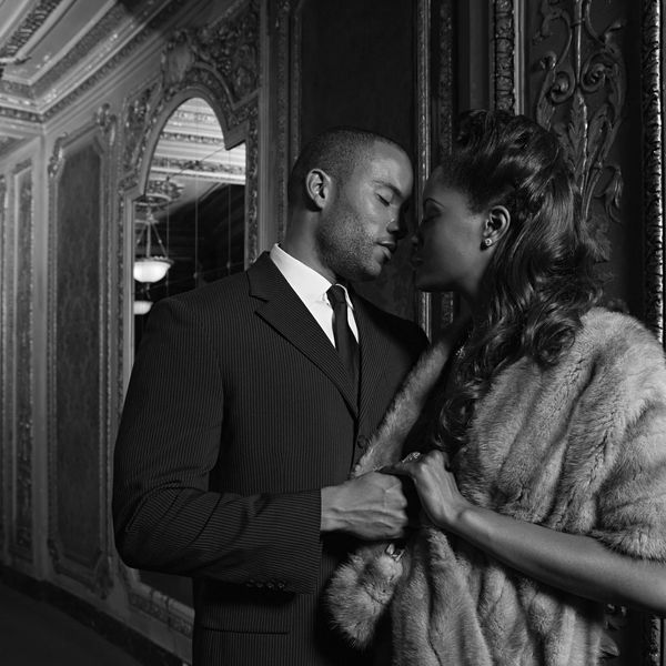 Couple embraces intimately in elegant, vintage setting.