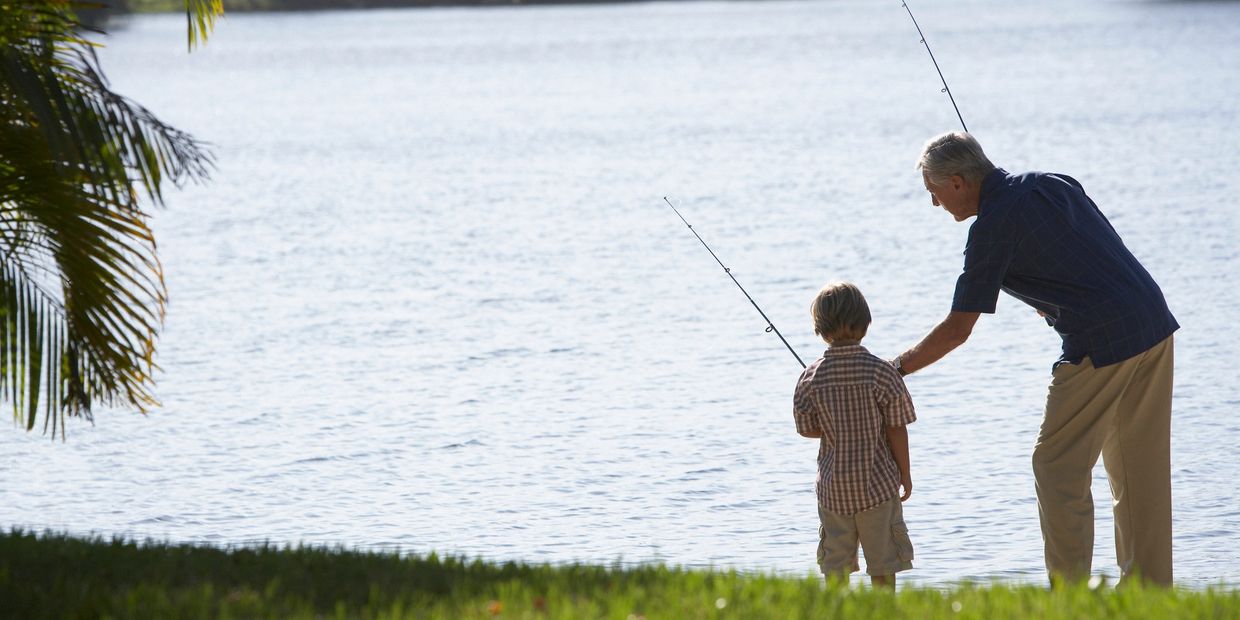 An elderly man teaching a young boy to fish by the lake.