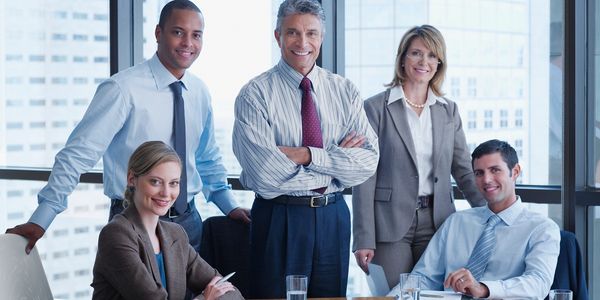A group of five diverse business professionals smiling in a modern office.