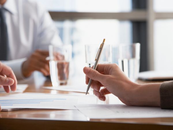 Business meeting with hands holding a pen and documents on the table.