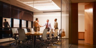 Three men shaking hands in a modern office conference room.