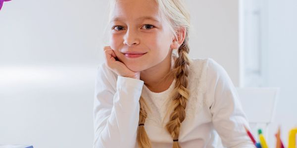 Young girl with braided hair reading a book at a desk with school supplies.