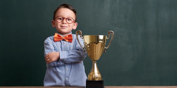 Young boy proudly stands next to a large trophy with arms crossed.