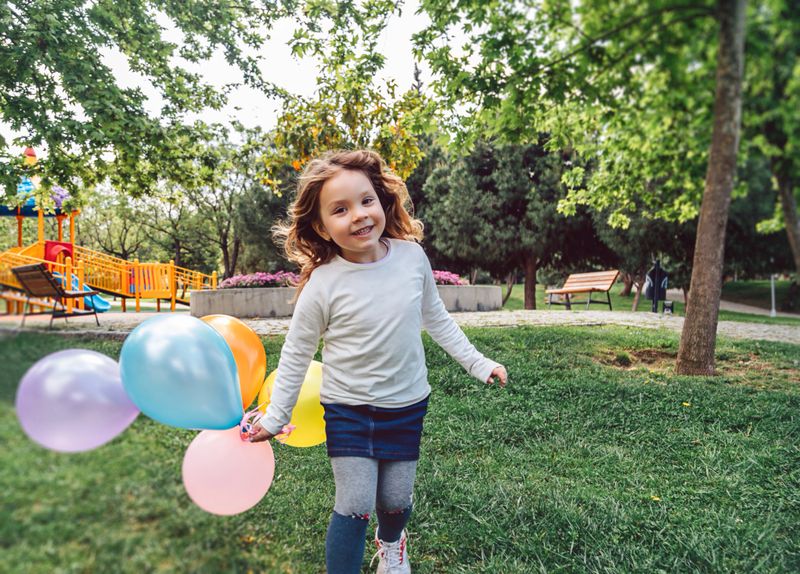 Smiling child in a colorful park, joyfully playing with a red balloon.