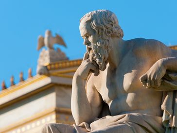 Marble statue of a contemplative bearded man against a blue sky.