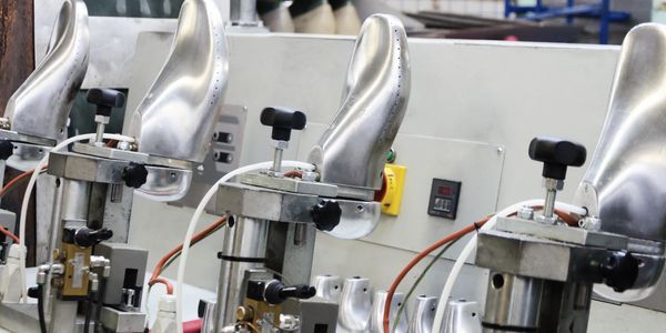 Metal shoe molds lined up on a shoe manufacturing machine.