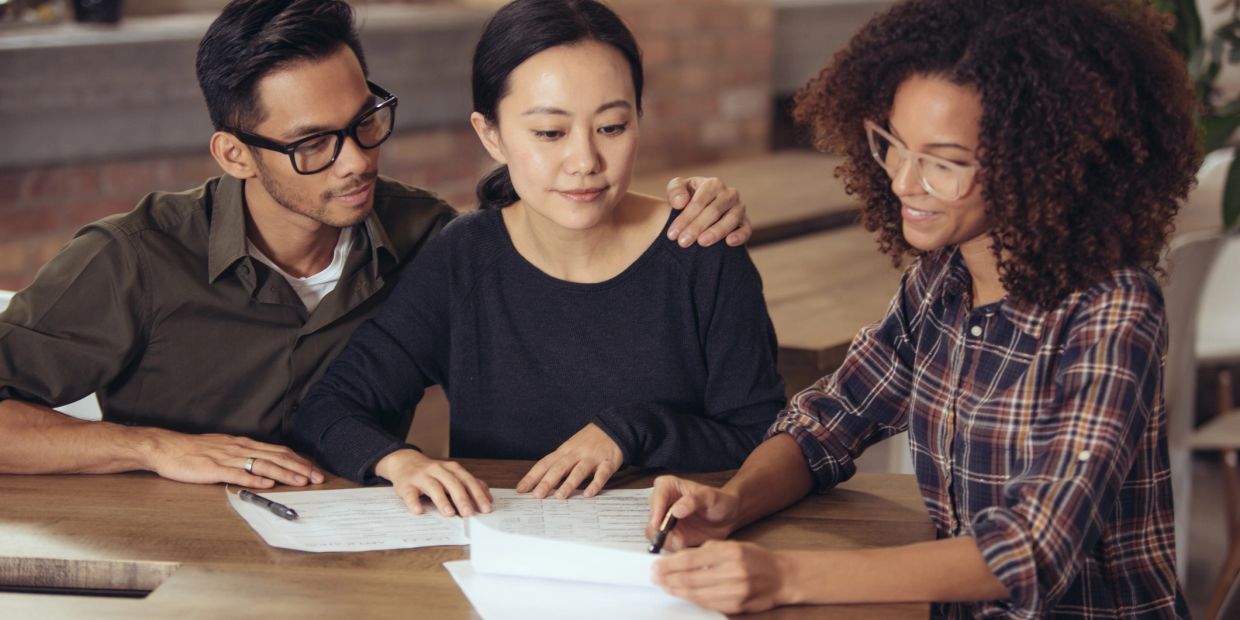 A couple discussing documents with a professional woman at a table.