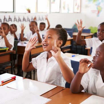 Happy children raising hands in a classroom.