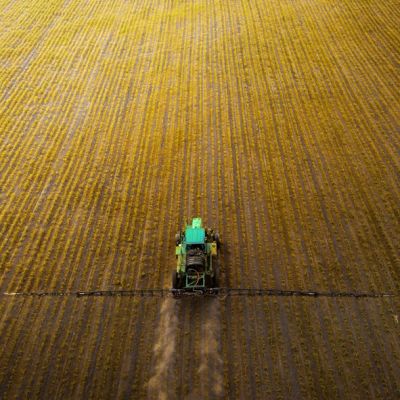 A tractor working on a vast, golden crop field from an aerial view.