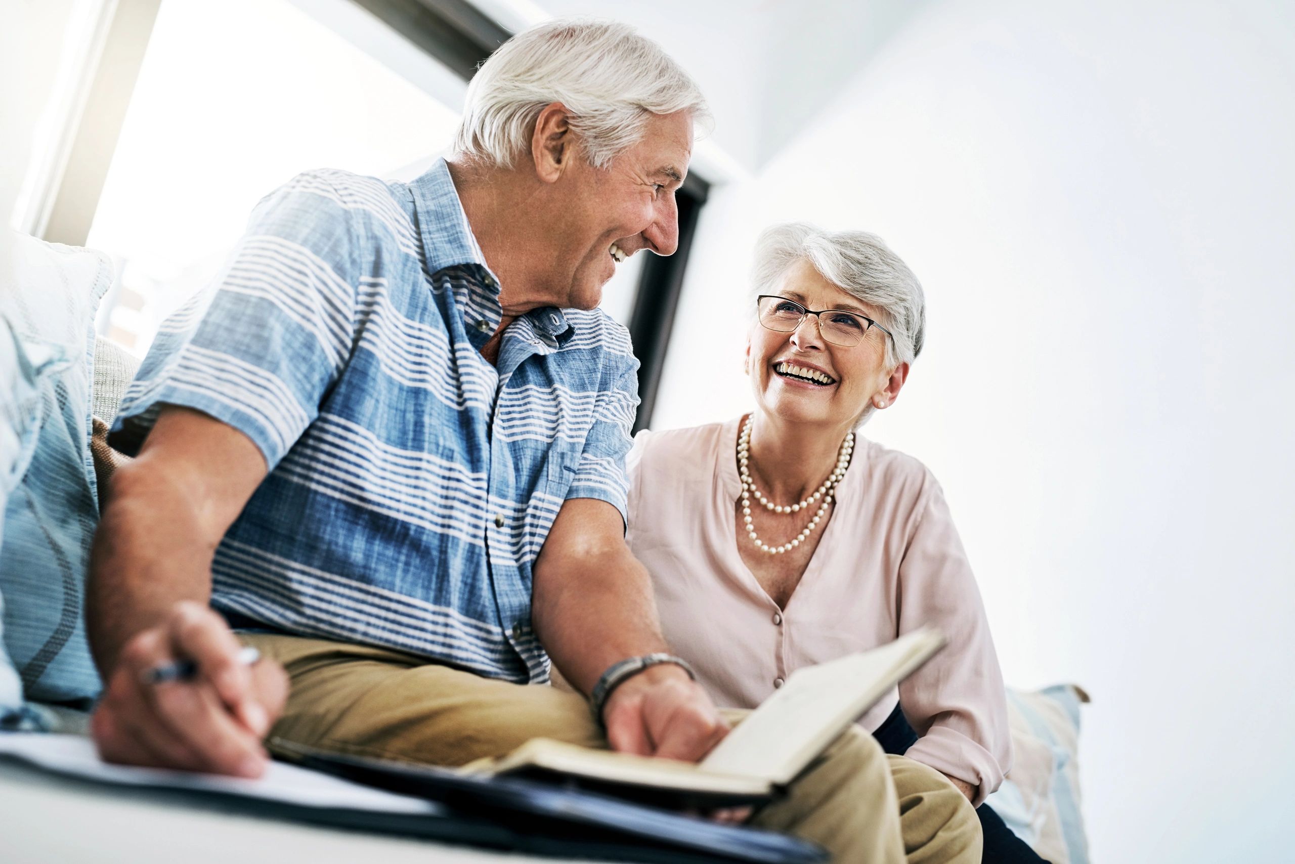 Elderly couple smiling and discussing while reviewing documents.