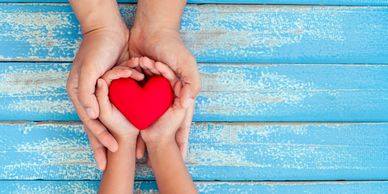 Photo of two sets of hands holding a red heart. 