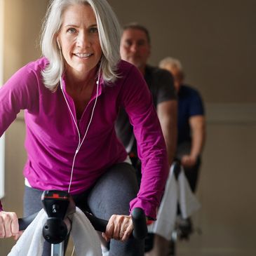 Mature woman enjoying a spin class with others indoors.