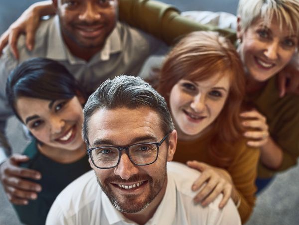 A diverse group of five smiling adults posing closely together.