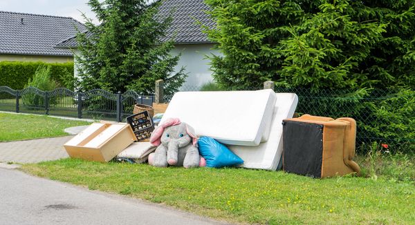 Discarded furniture and a large stuffed elephant toy by the roadside.
