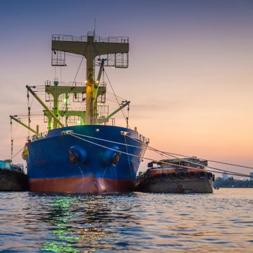 Large blue cargo ship docked at sunset with calm water reflecting lights.