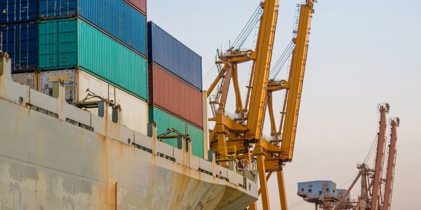Cargo containers stacked on a ship being loaded by cranes at a port.