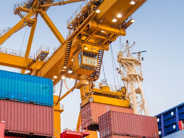 A large yellow crane lifting shipping containers at a port.