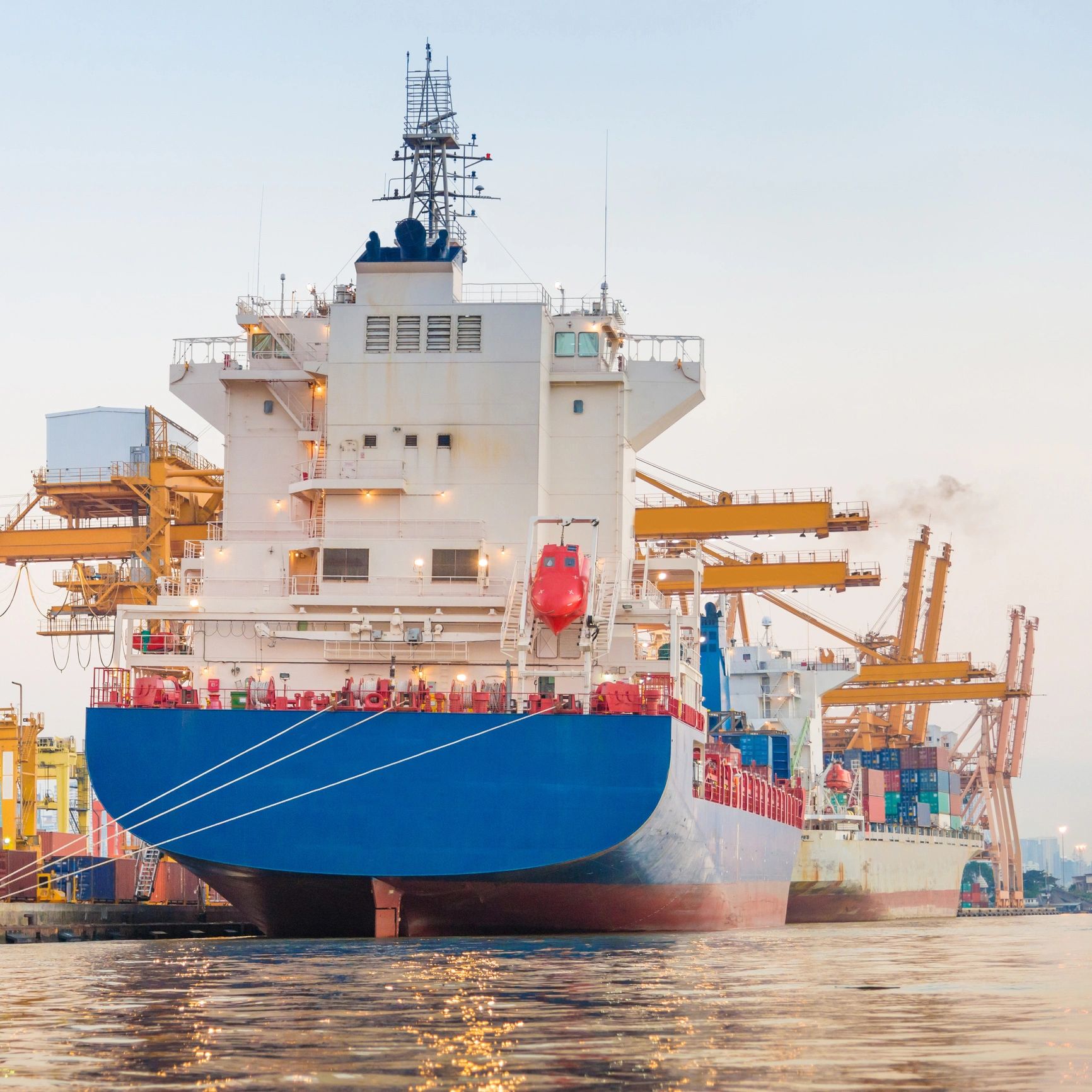 Large cargo ship docked at a busy port with cranes in the background.