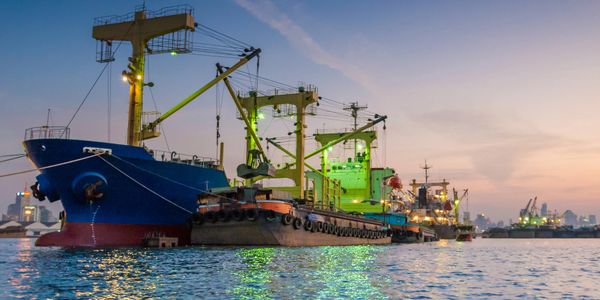 Large cargo ships docked at a harbor during twilight.