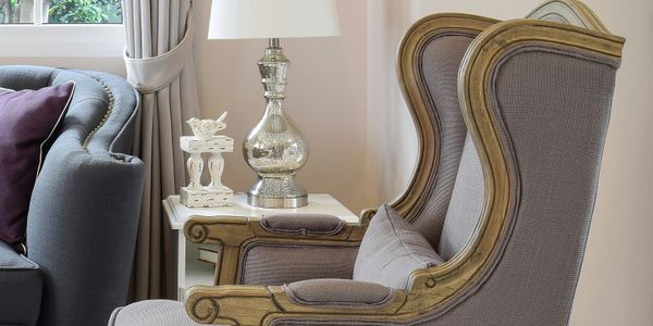 Elegant gray armchair with wooden frame next to a side table and lamp.