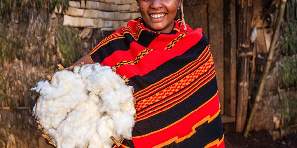 Woman in traditional attire holding a basket of cotton and smiling.