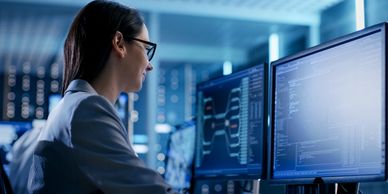 Woman analyzing data on computer screens in a tech environment.