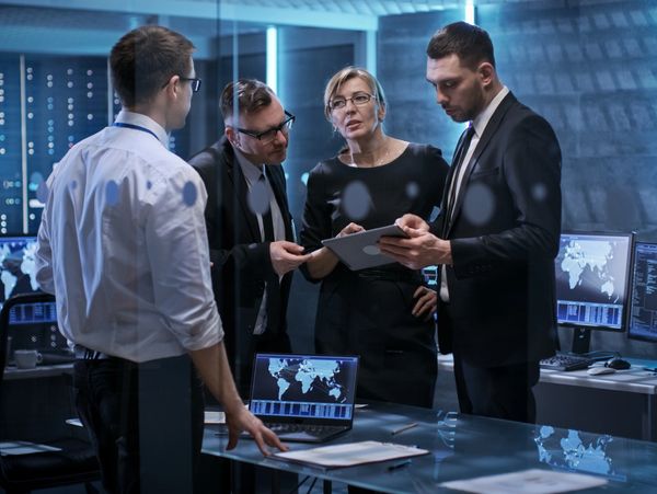 Four professionals discussing data on a tablet in a high-tech office.