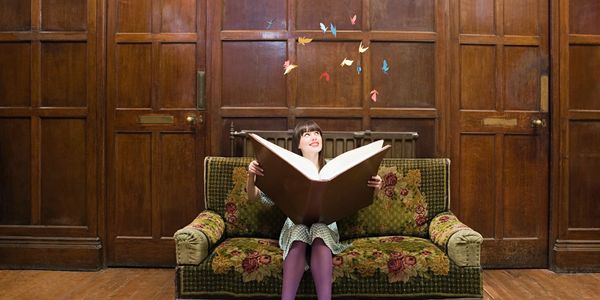 Girl reading giant book with butterflies flying out.