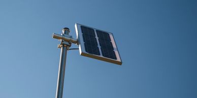 A small solar panel mounted on a metal pole against a clear blue sky.