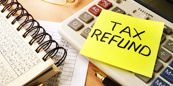Sticky note with 'Tax Refund' on a calculator and financial documents.