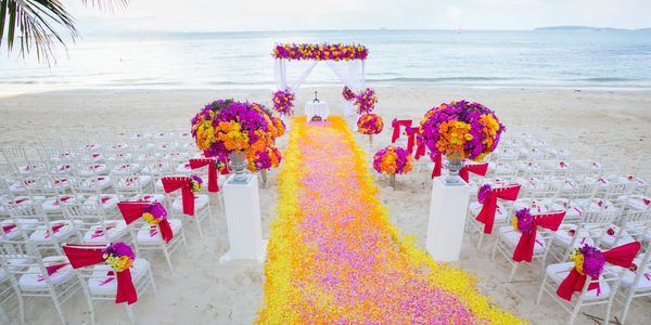 A vibrant beach wedding setup with colorful flower decorations and white chairs.
