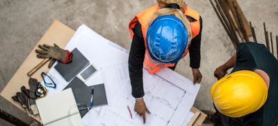overhead photo of two construction workers wearing hard hats looking at a set of plans on a job site