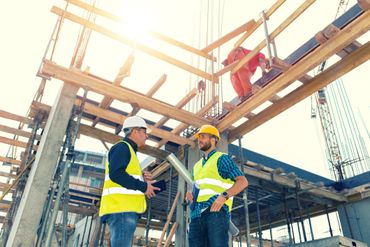 Two construction workers discussing plans at a building site during daytime.