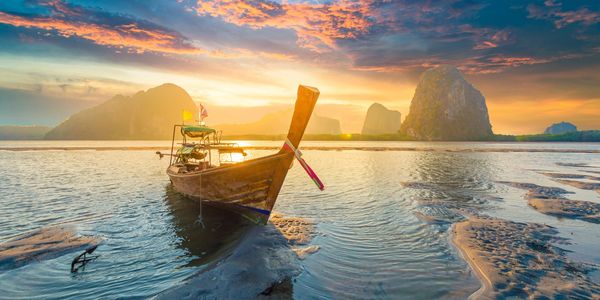 Traditional wooden boat on shallow water at sunset with limestone cliffs.