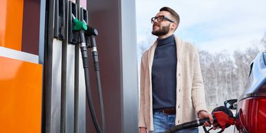 Man refueling his car at a gas station on a clear day.