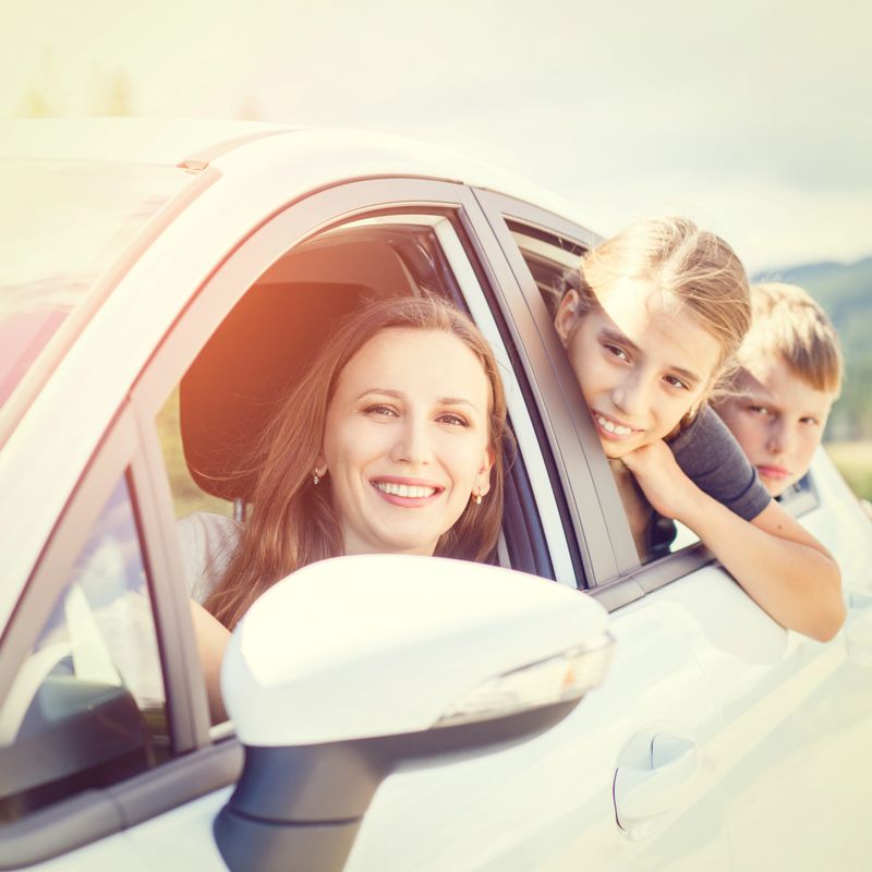 Happy young woman and her children sitting in a car and look out from windows. Family travel warm color toned image
