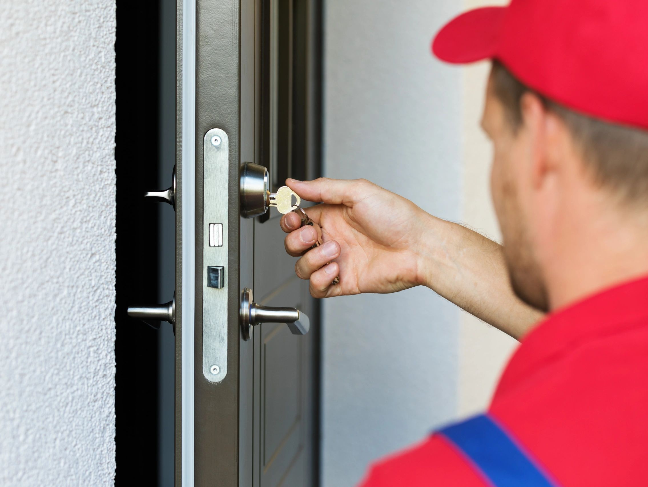 A person in a red cap unlocking a door with a key.