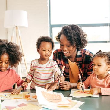 A woman and three young children drawing together at a table.