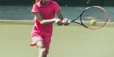 Young girl in pink outfit playing tennis on an outdoor court.