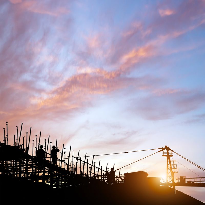 Construction site, silhouettes of construction industry workers on scaffolding against the sunset light.