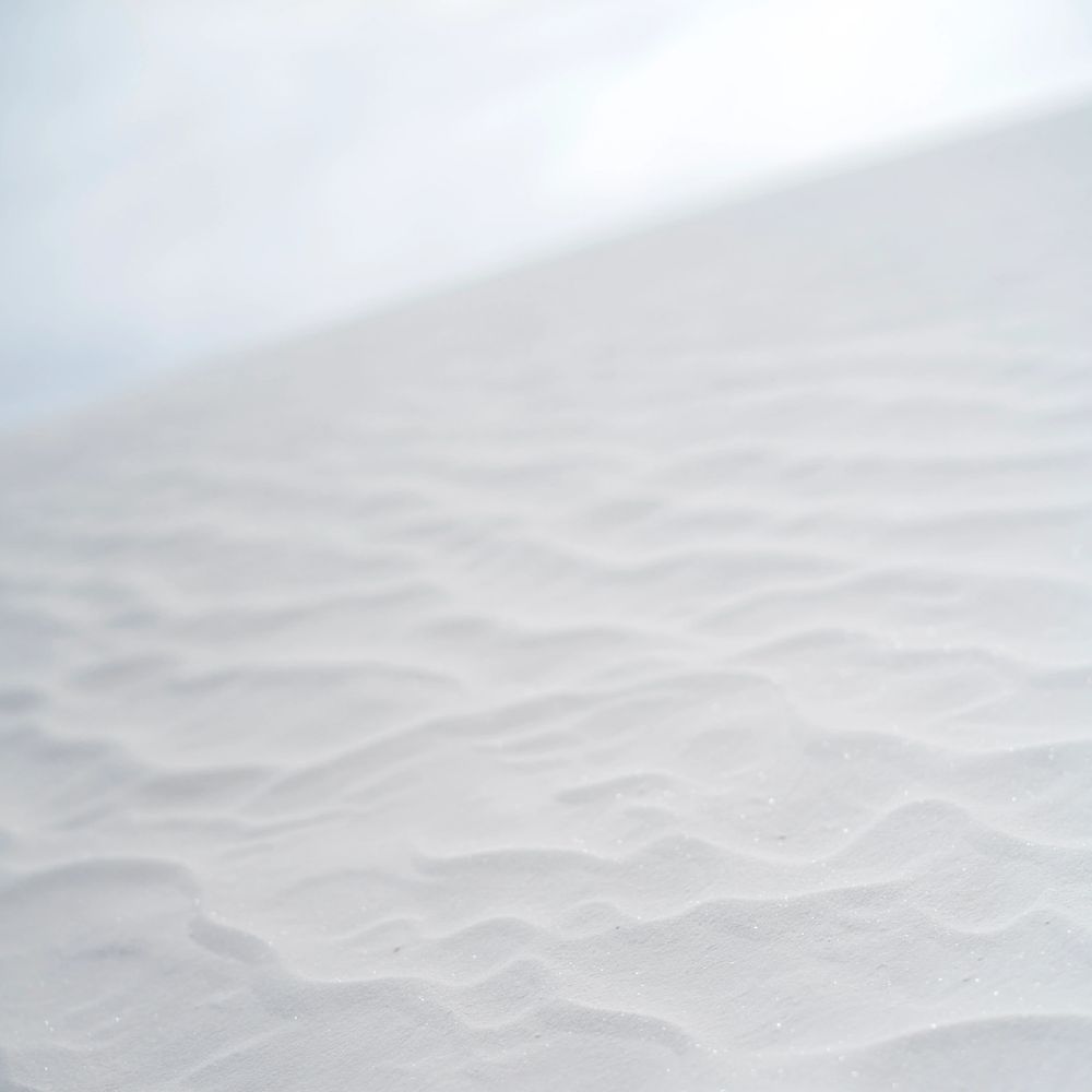 Close-up of white sand dunes with textured ripples under soft light.