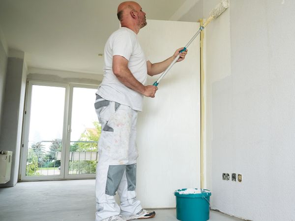 Man painting a white wall with a roller in an empty room.